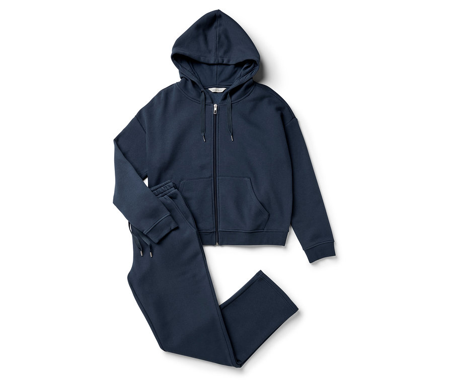 Egy sötétkék, cipzáros kapucnis pulóver és egy tréningnadrág fekszik egy fehér háttéren.