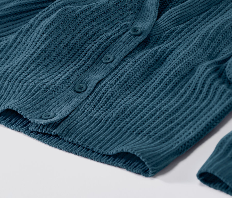 Közelkép egy gombos, petróleum színű kötött kardigánról.