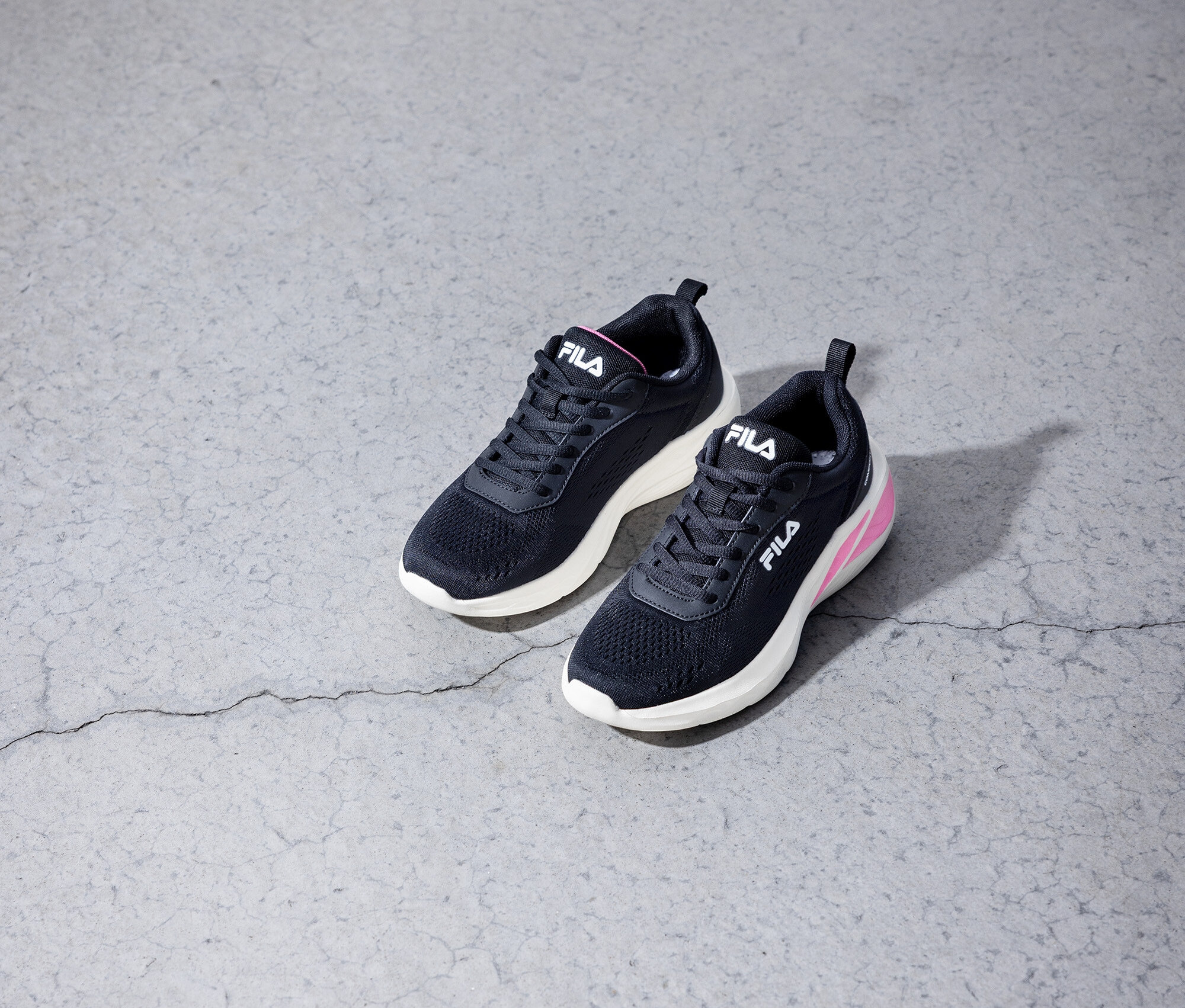 Két fekete Fila sneaker cipő fekszik egy szürke beton padlón.