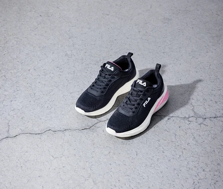 Két fekete Fila sneaker cipő fekszik egy szürke beton padlón.