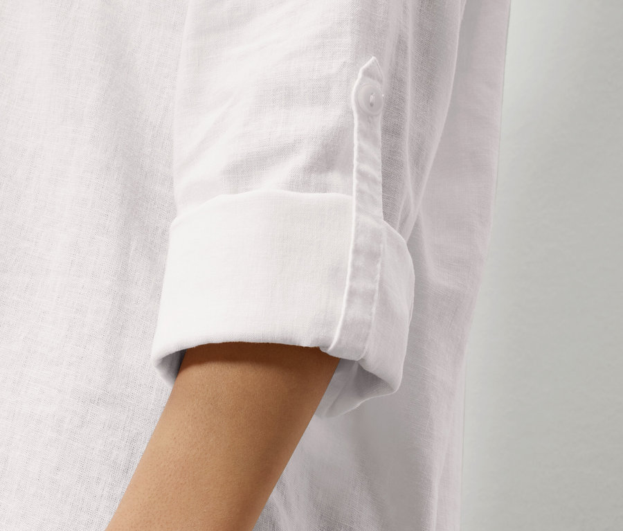 Egy fehér lenvászon ing ujjának közeli képe felhajtott ujjal és egy gombbal.