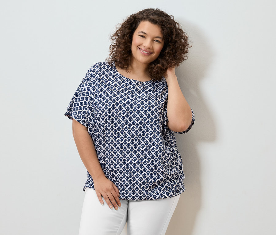 Mosolygó, göndör hajú nő kék-fehér blúzban és fehér nadrágban.