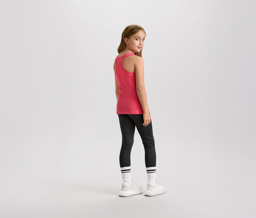 Egy fiatal lány visszanéz a válla fölött, rózsaszín trikót, leggingst és fehér tornacipőt visel.