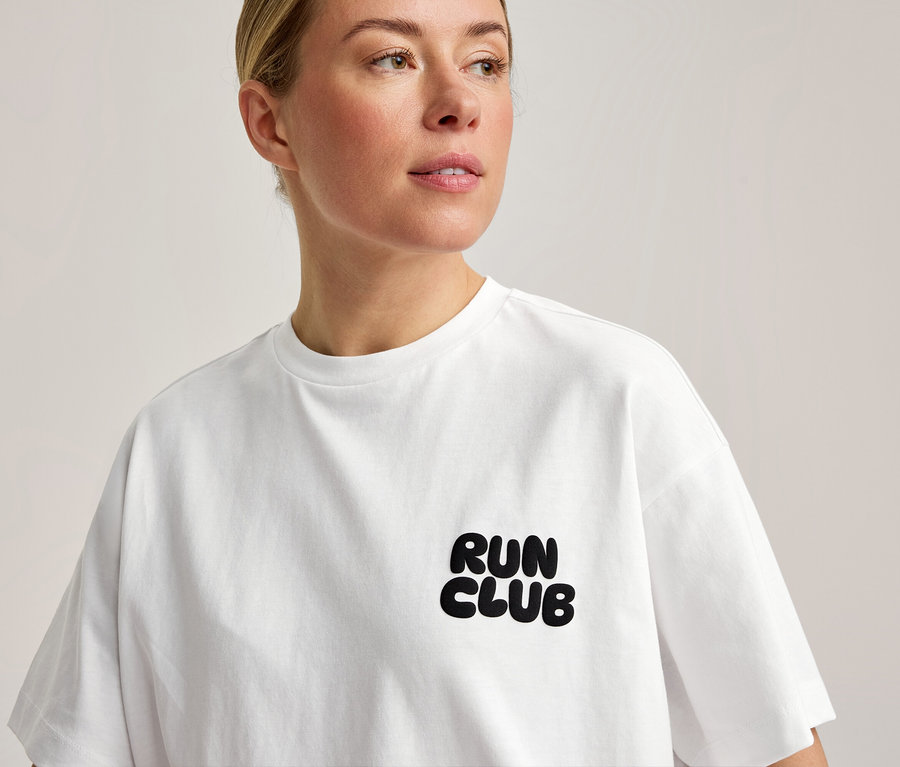 Egy nő fehér Sportfelsőt visel, mellkasán „RUN CLUB” felirattal.