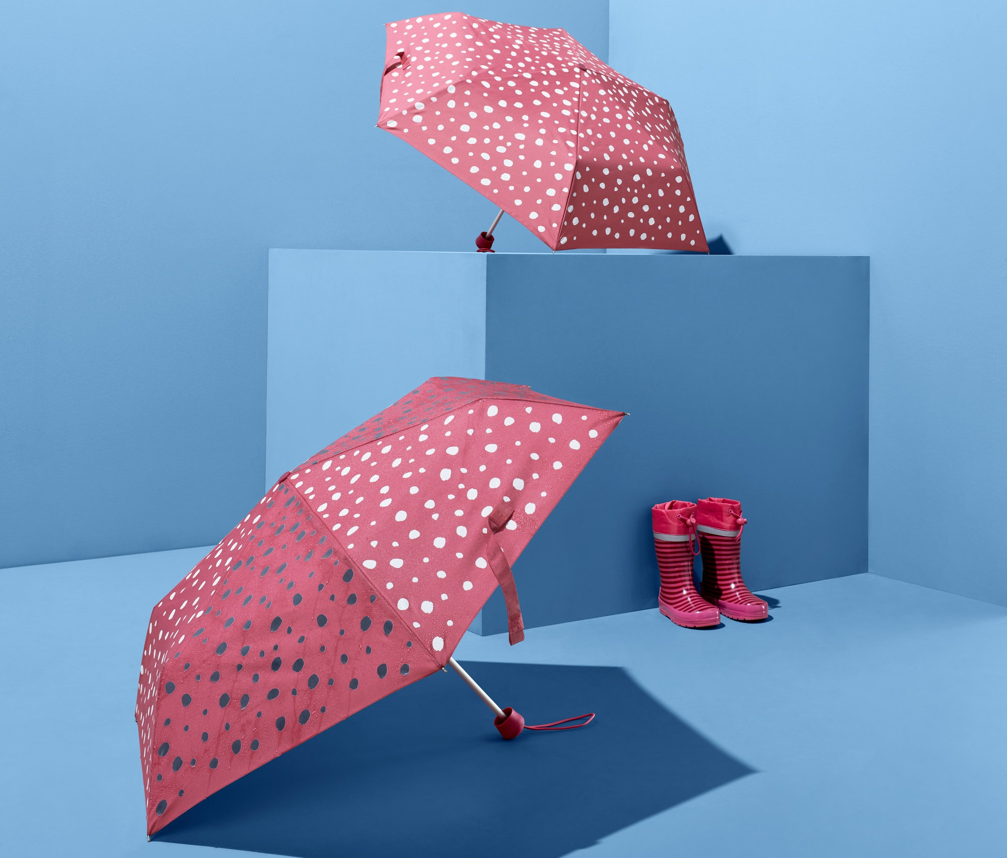 Két színváltós esernyő és egy pár gyermek gumicsizma kék háttér előtt.
