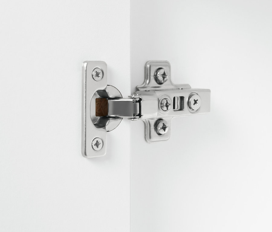 Egy ezüst színű zsanér részlete egy fehér, kétszárnyú fürdőszobai szekrényen.