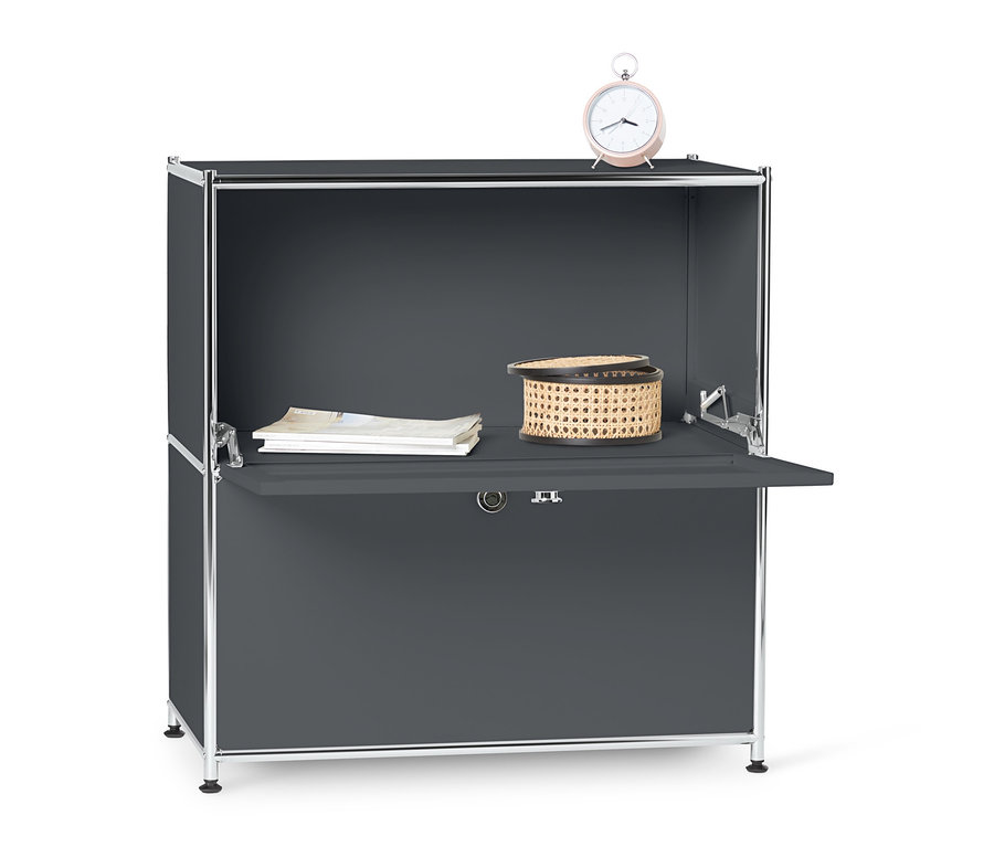 Szürke fém komód, 2 ajtóval, a tetején fonott kosár, dokumentumok és egy rózsaszín ébresztőóra.