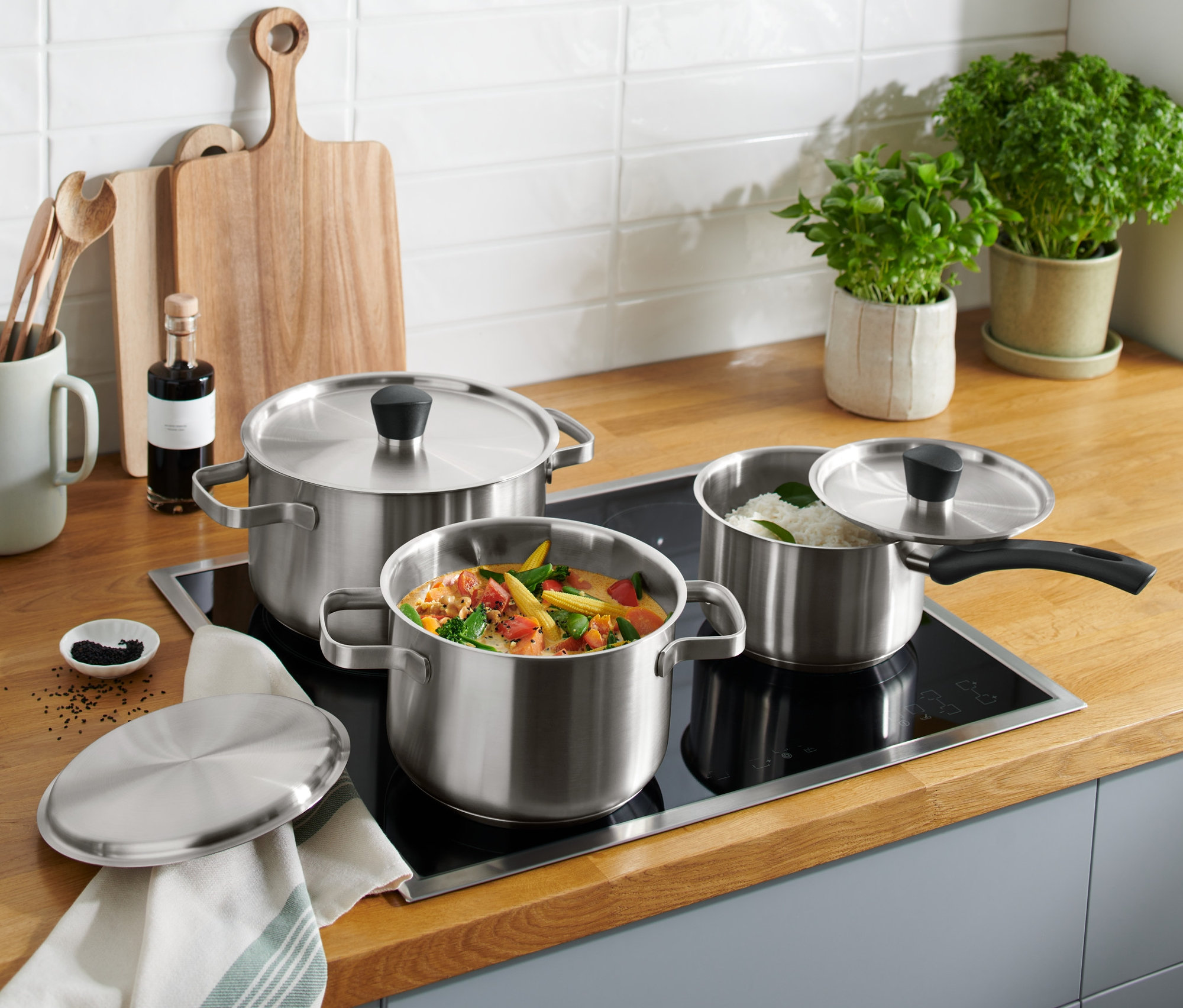 Rozsdamentes acél edénykészlet az indukciós főzőlapon, az egyikben zöldség, a másikban rizs.