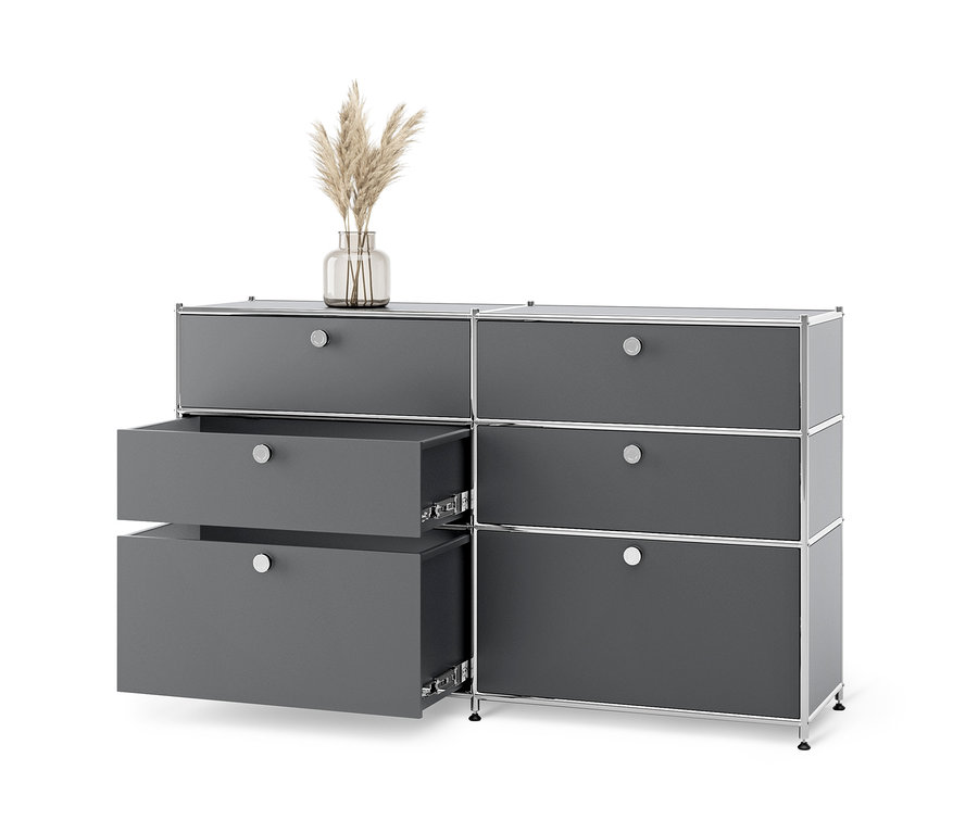 Szürke »CN3« fém komód 6 fiókkal, melyből kettő nyitva van, és egy váza fűvel a tetején.