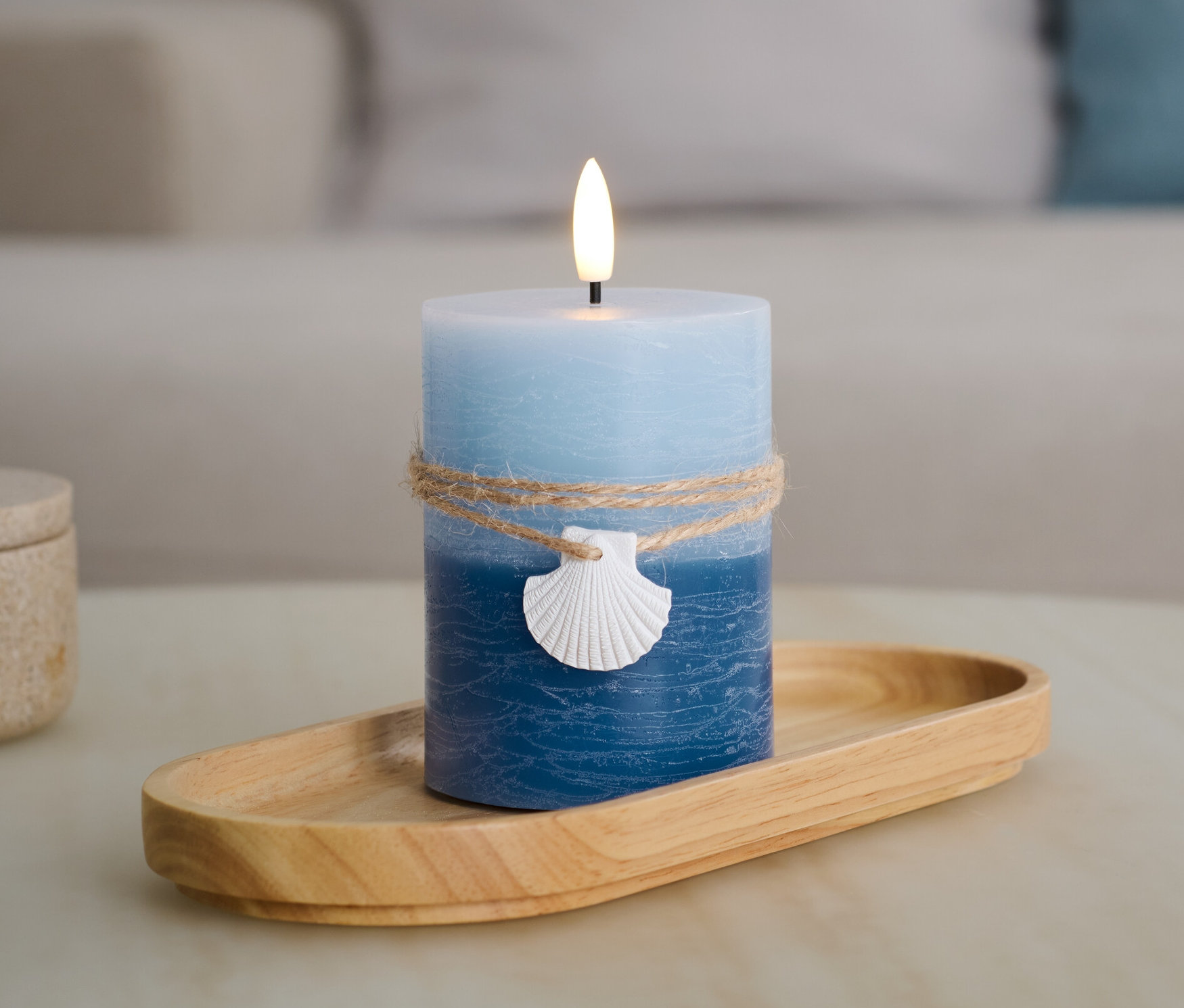 Egy kék LED-es valódi viaszgyertya, kagylóval, egy fa tálcán.