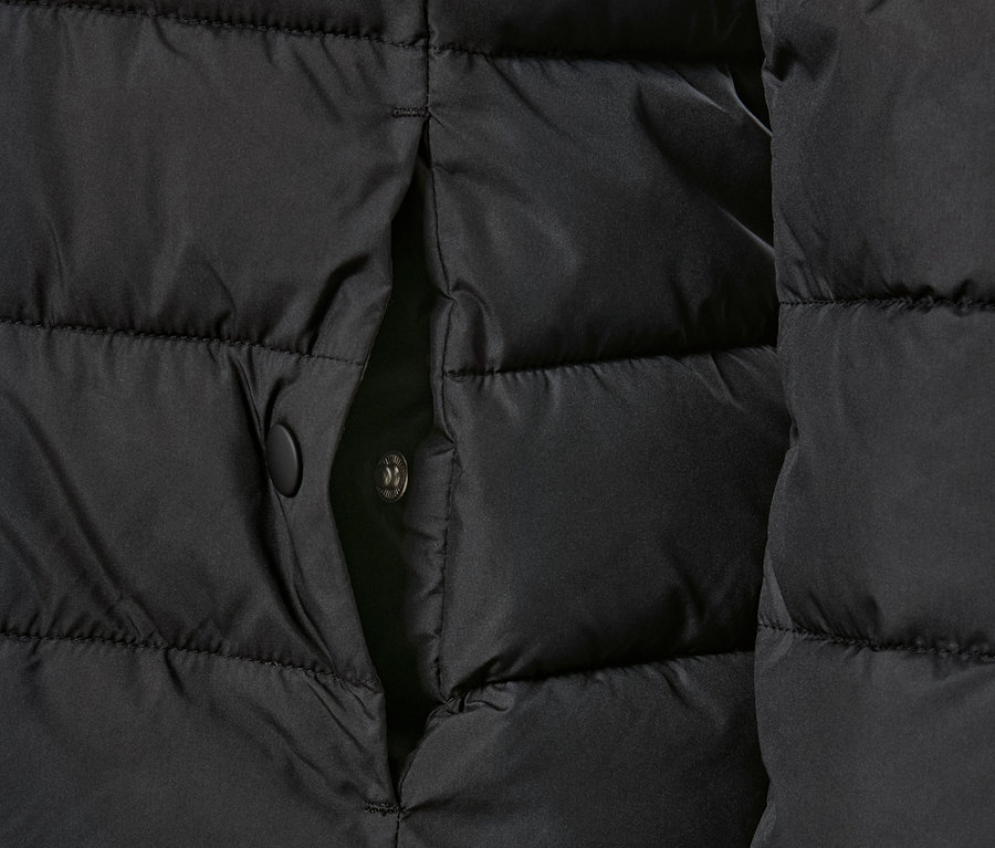 Egy fekete, kapucnis, steppelt kabát részlete patenttal.