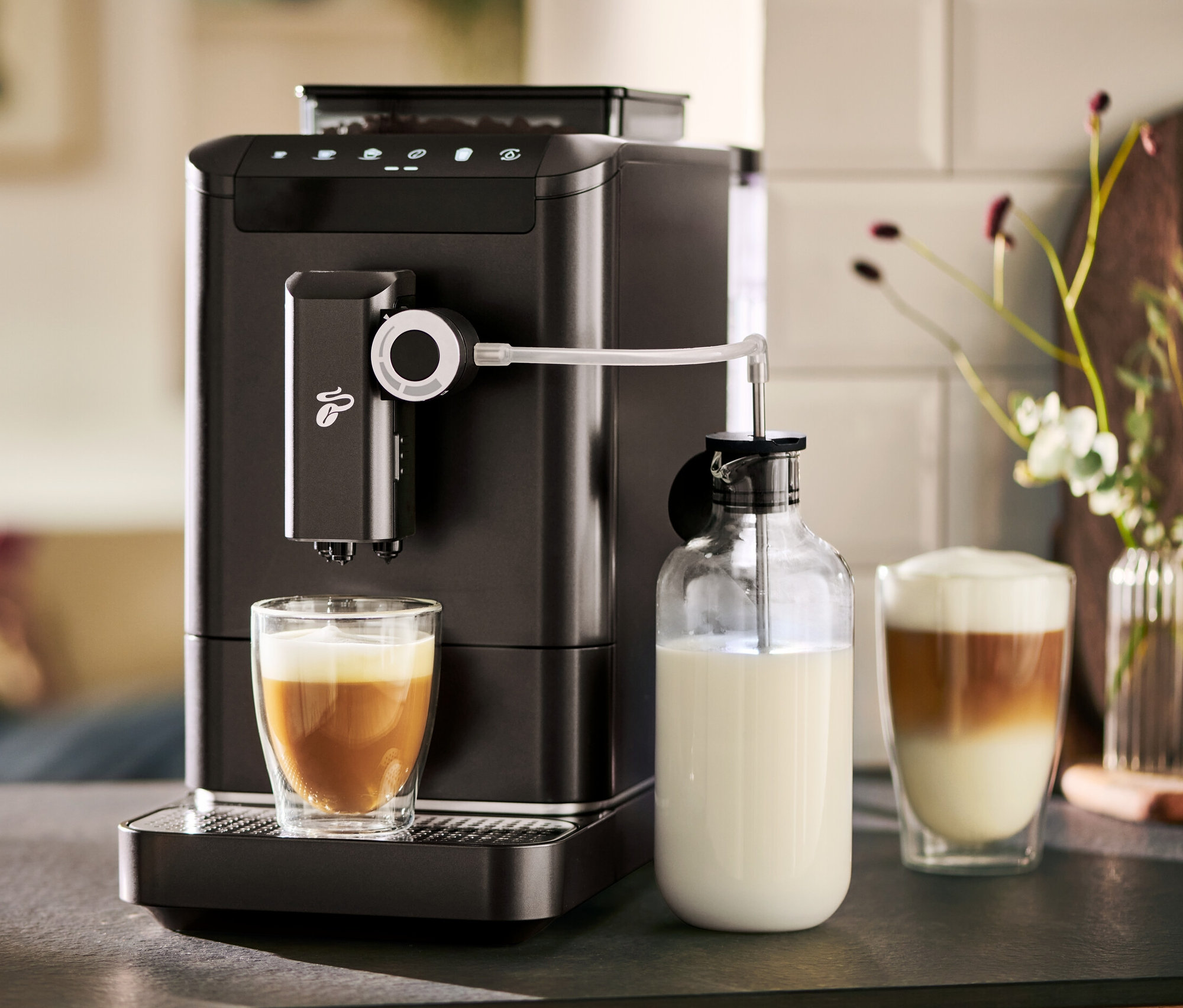 A »Esperto 2 Milk« Granite Black automata kávéfőző kávét készít egy pohárba. Mellette egy tejeskancsó áll.