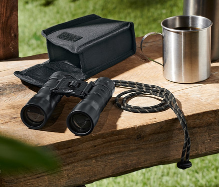 Egy »12x32« zseblátcső egy tok, egy termosz és egy csésze mellett fekszik egy fából készült padon.