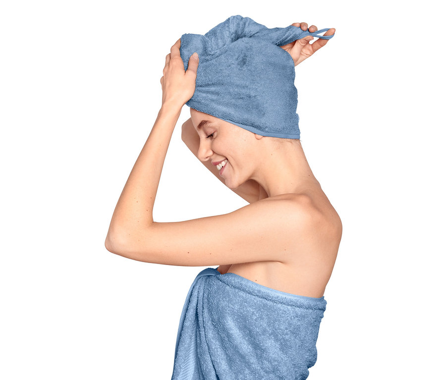 Egy nő turbán alakú törölközőt igazít a fején, a teste köré törölköző van tekerve.