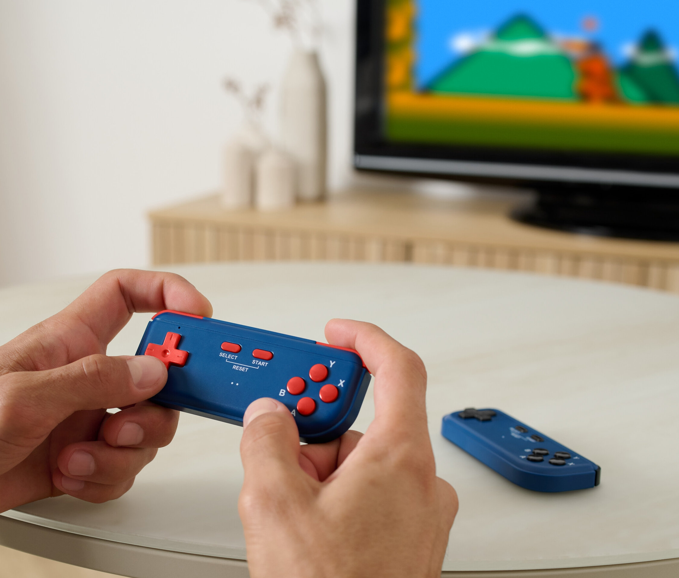 Egy férfi mini retro játékkonzolon játszik, a háttérben egy tévé látható.