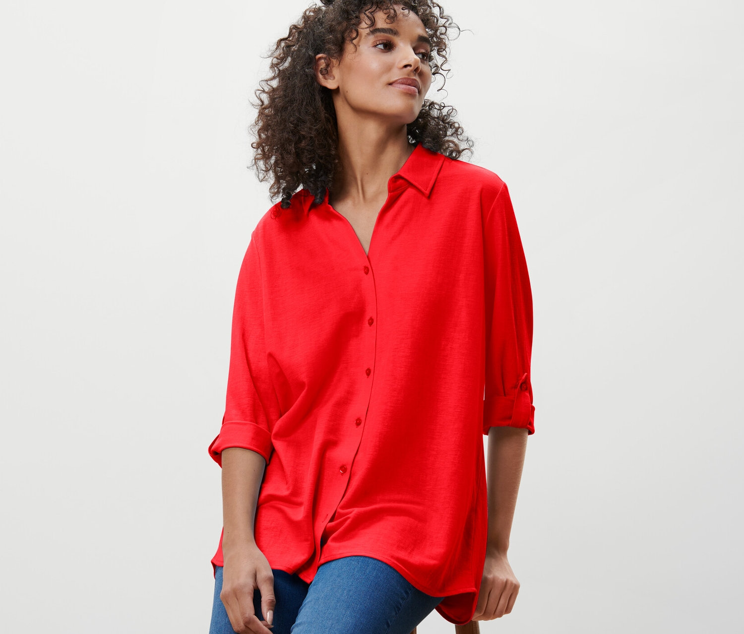 Nő ül egy széken, piros piké jersey blúzban.