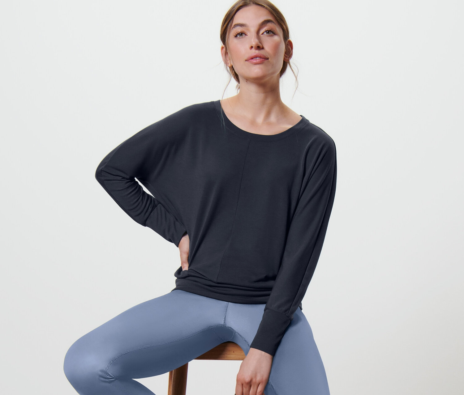 Nő ül a széken, sötétkék női denevérujjú sportfelsőt visel.