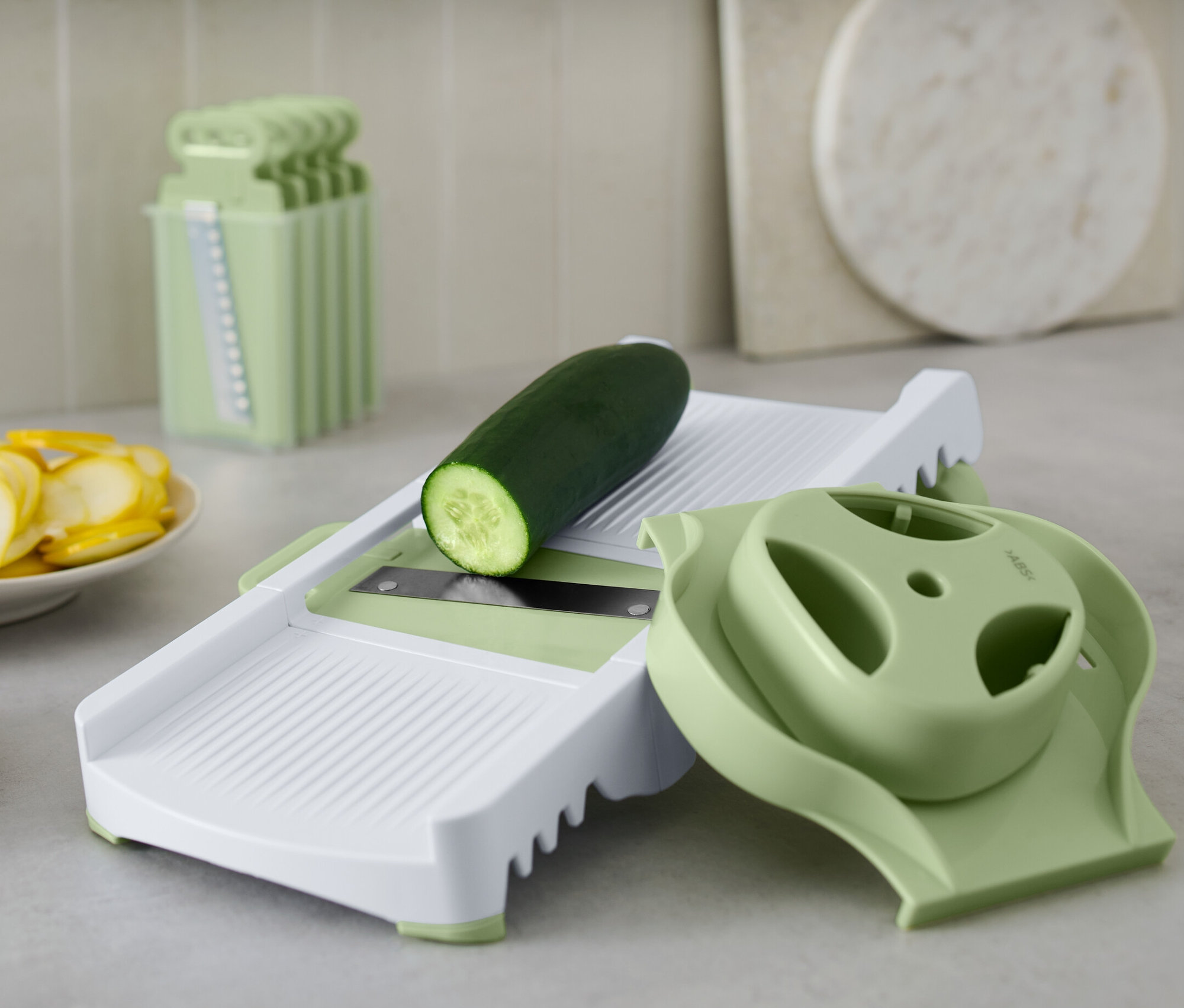 Uborka fekszik a multifunkciós reszelőn. Mellette szeletelt uborka és cukkini látható.