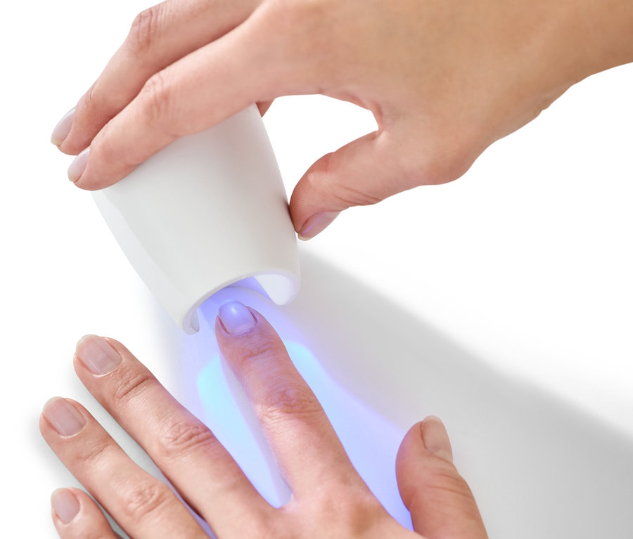 Nő használja az UV lámpát egy manikűr- és pedikűrkészletből.