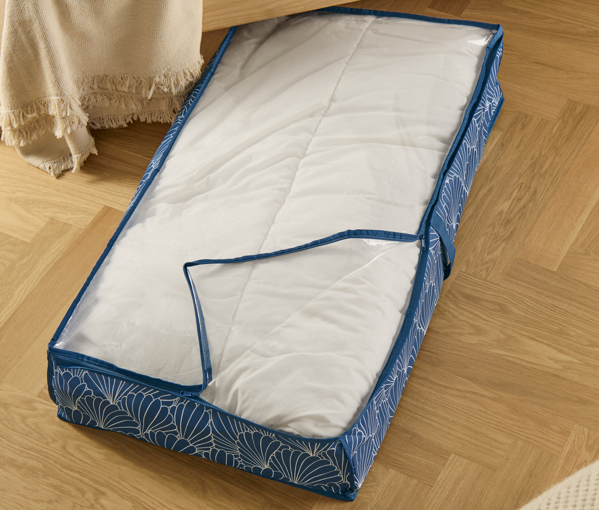 Kagylós mintájú, kék ágy alatti tároló (95 x 18 x 50 cm) részben átlátszó, parkettán.