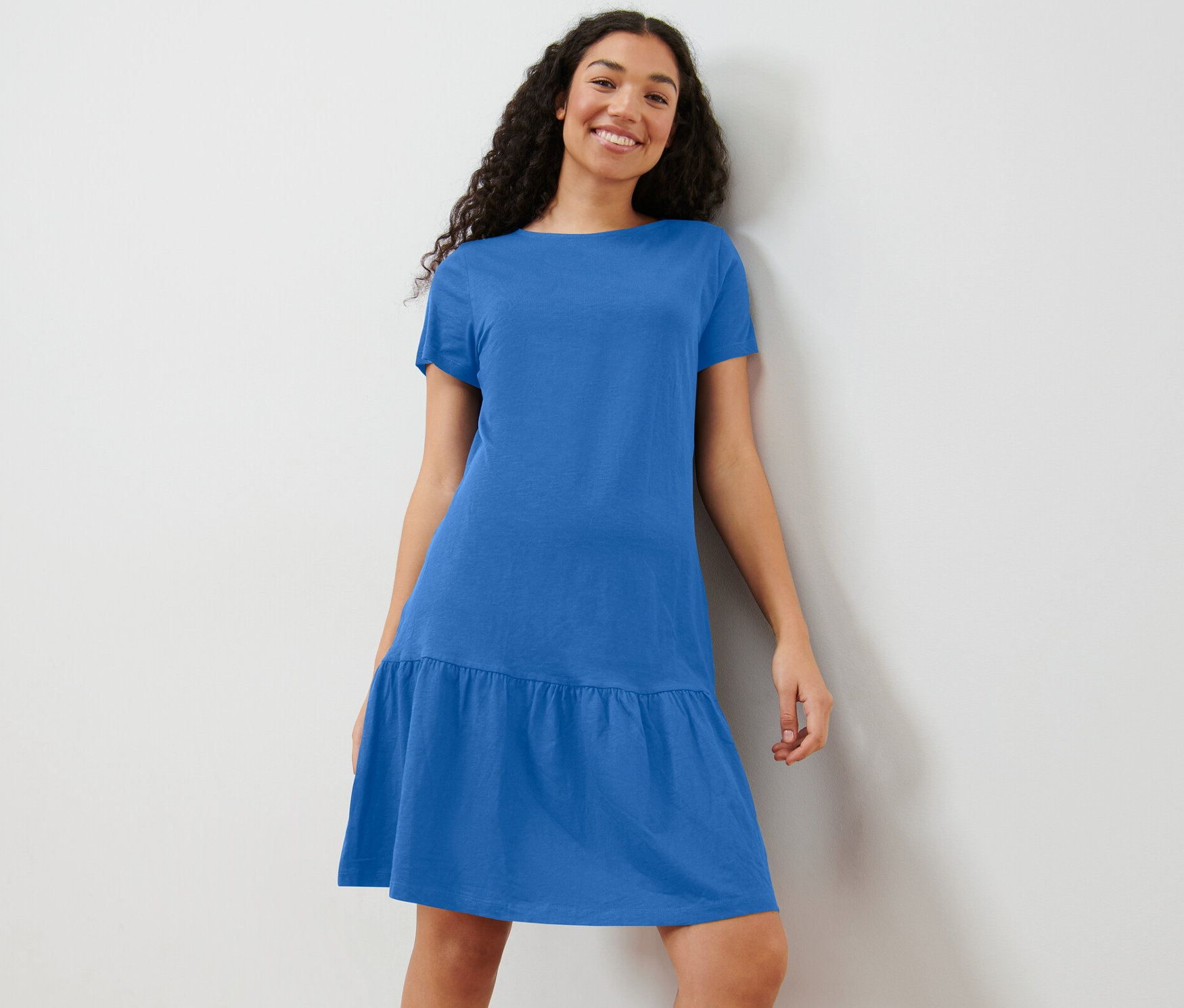 Nő pózol kék jerseyruhában.