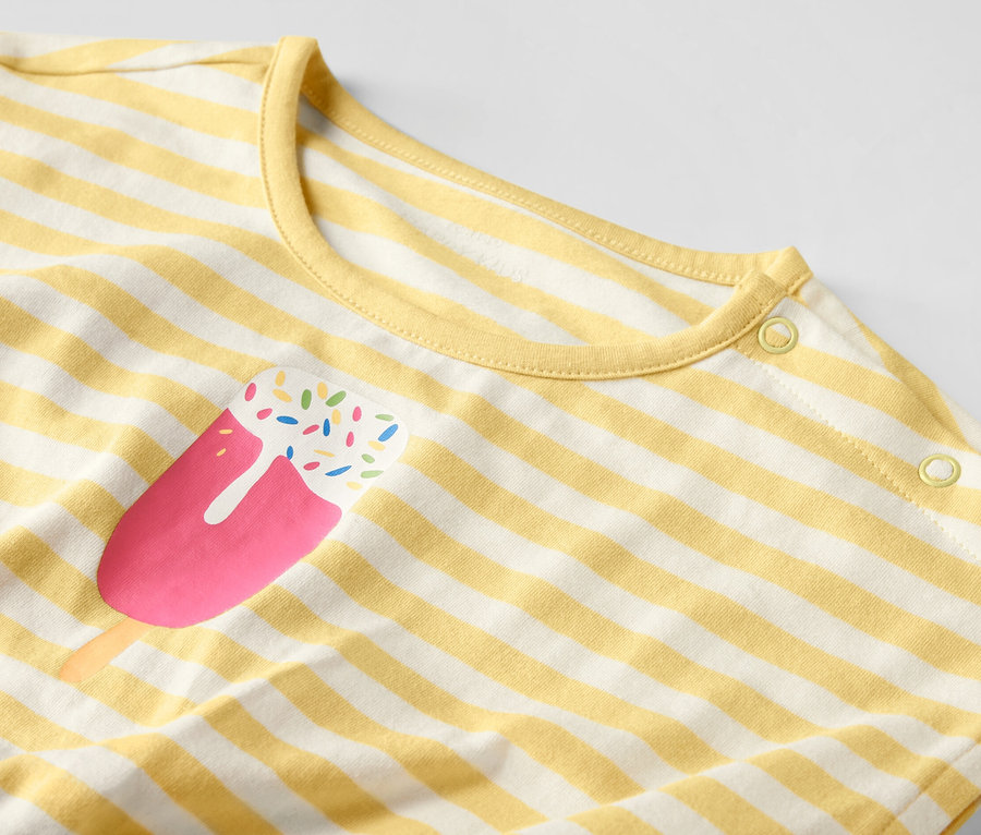 Egy sárga-fehér csíkos, jégkrém mintás gyerek kezeslábas részlete.