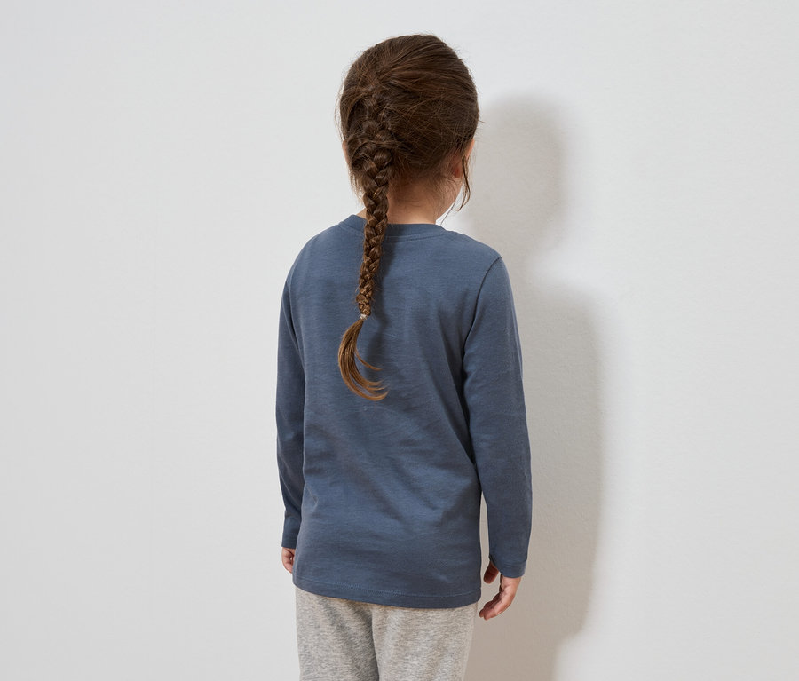 Hátulról látható egy barna hajú lány, haja fonatba van fonva. Kék, hosszú ujjú pólót és szürke melegítőnadrágot visel.