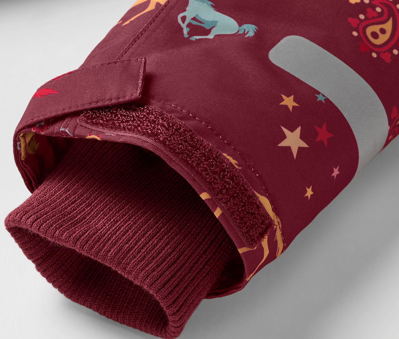 Egy bordó kabátujj részlete ló- és csillagmintával, bordó szegéllyel.