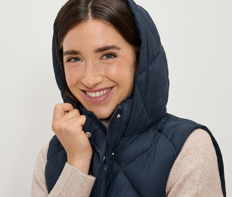 Mosolygó nő sötétkék, steppelt mellényt visel kapucnival.
