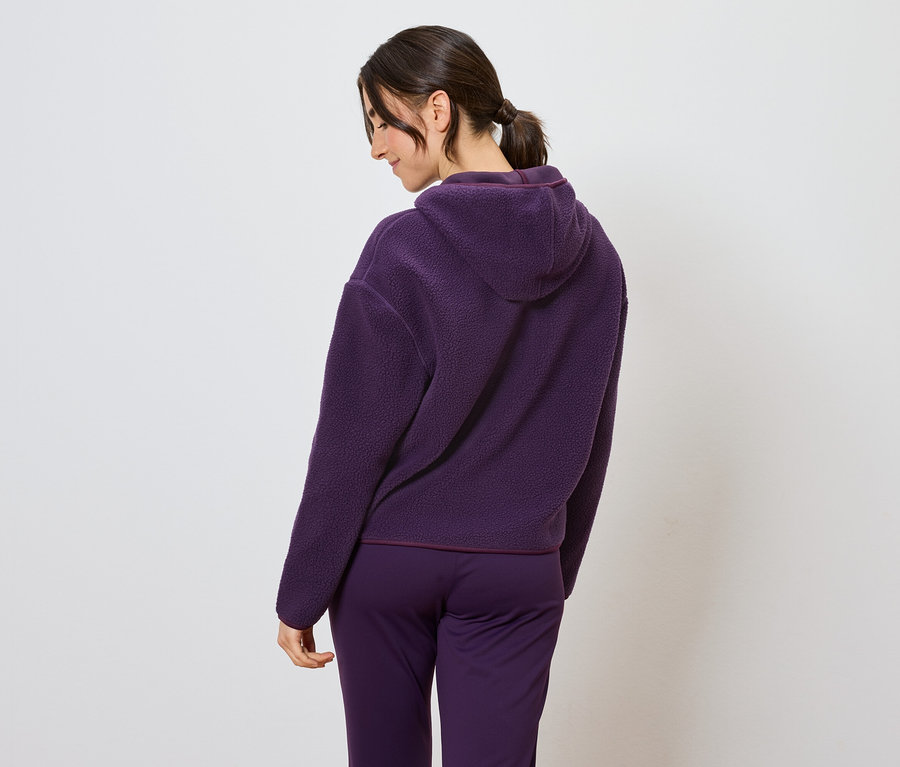 Hátulnézetből látható nő lila kapucnis tréningruhában.