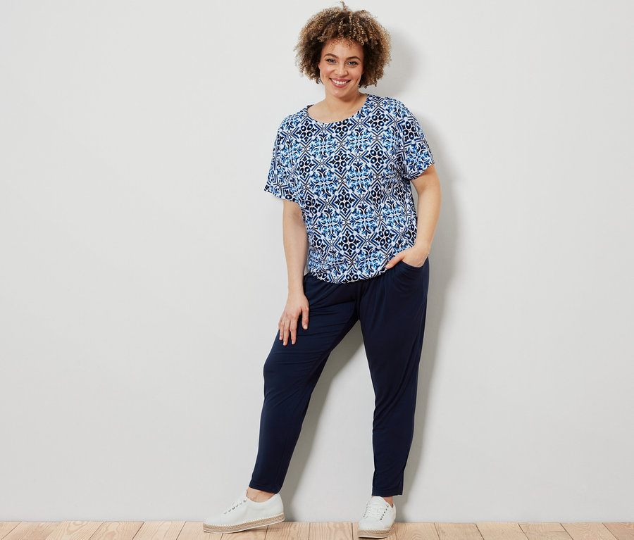 Nő pózol kék, mintás pólóblúzban és sötétkék jersey nadrágban.