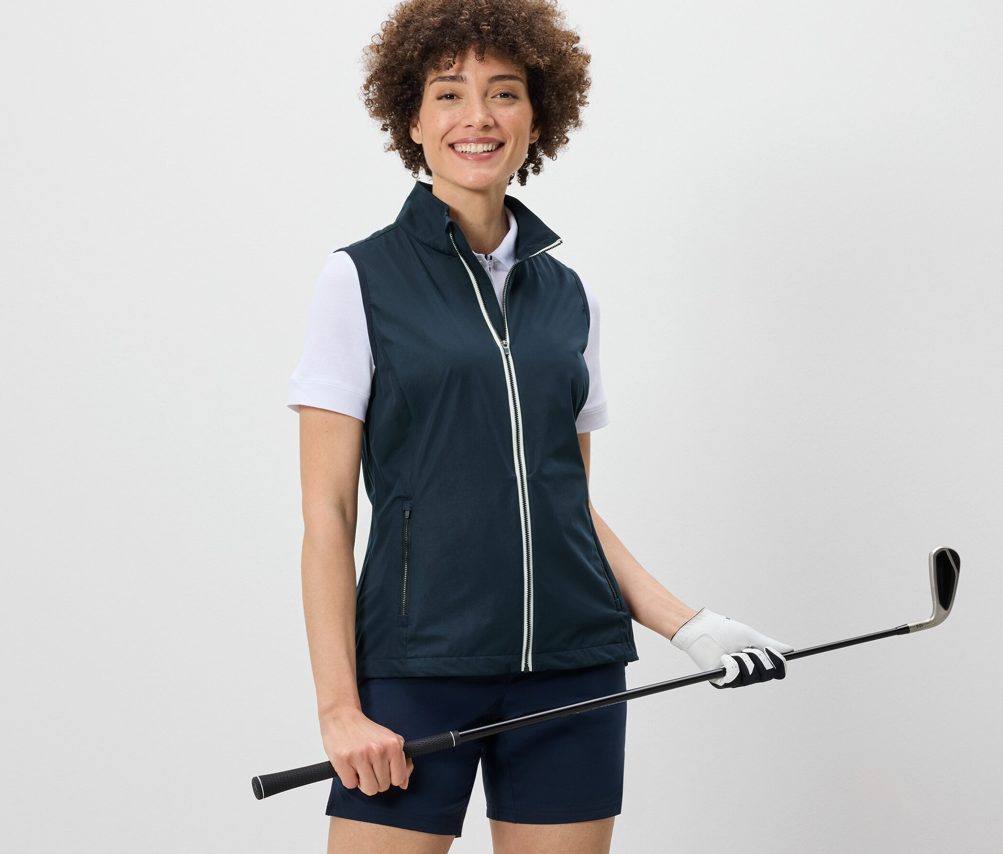 Nő softshell mellényt visel és golfütőt tart.