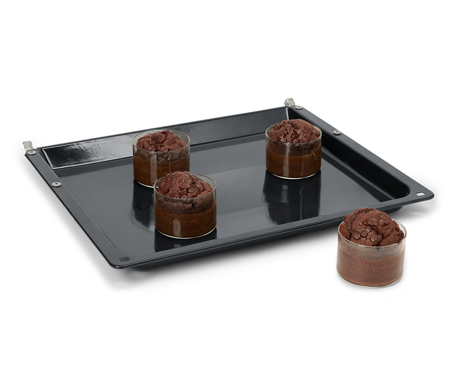 Négy csokoládés muffin üvegekben egy fekete sütőlemezen.