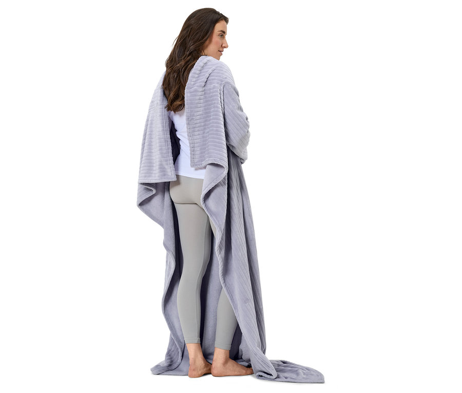 Egy nő áll háttal a kamerának, szürke takaróba burkolózva.