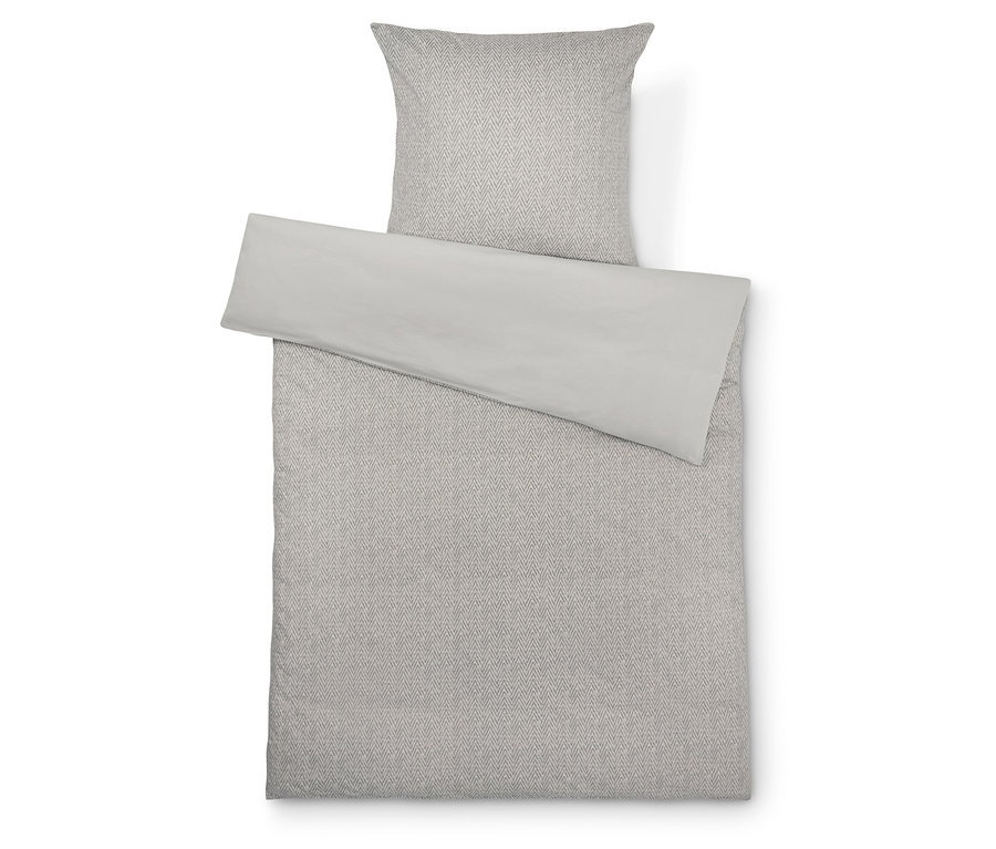 Ágynemű geometrikus mintával és világosszürke ágytakaróval.