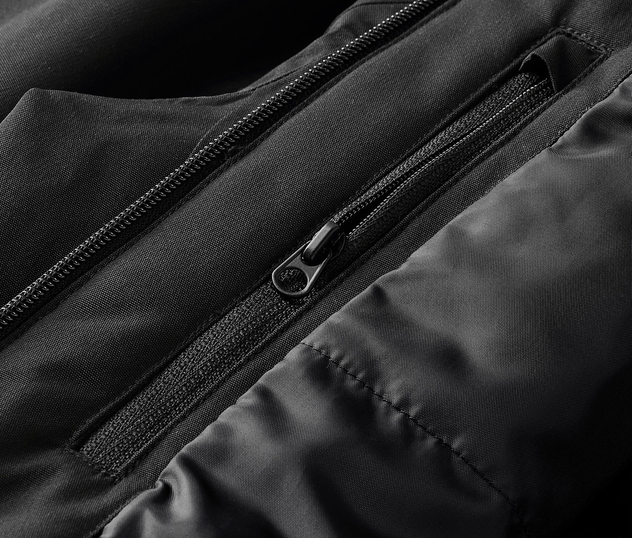 Egy fekete kabát részlete, látható cipzárakkal és steppeléssel.