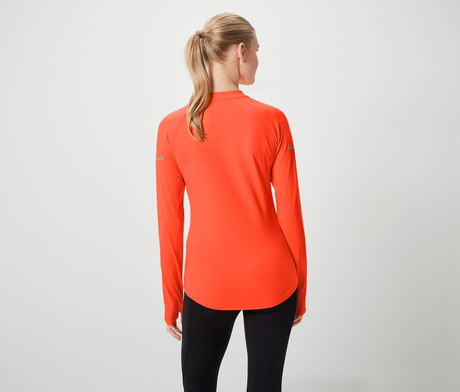 Hátulról látható egy szőke hajú, lófarokba kötött nő, aki narancssárga, hosszú ujjú sportfelsőt és fekete leggingst visel.