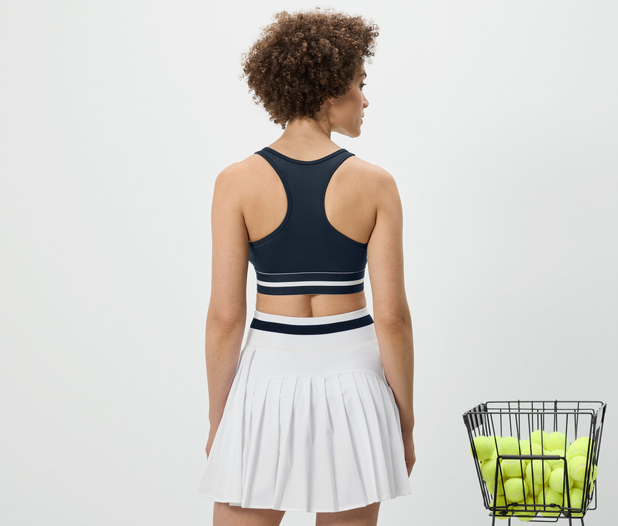 Hátulnézetből egy nő kék »Crop Top« sportmelltartót és fehér szoknyát visel.