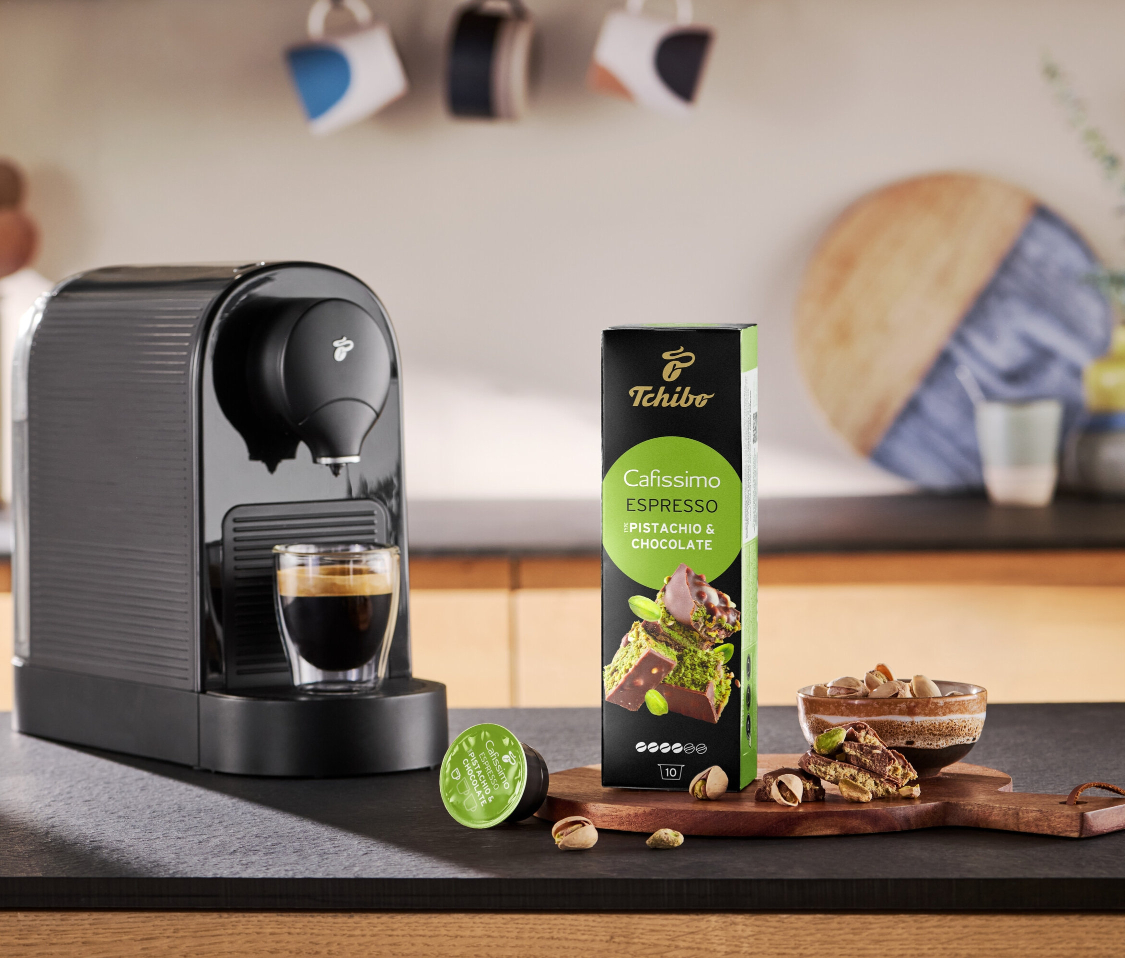 Kávéfőző kávét önt egy csészébe a Cafissimo Flavoured Espresso kapszulacsomag mellett.