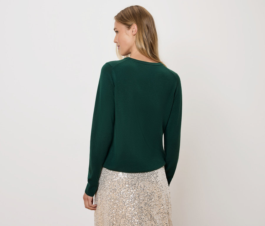 Nő néz a válla fölött, zöld pulóvert és flitteres szoknyát visel.