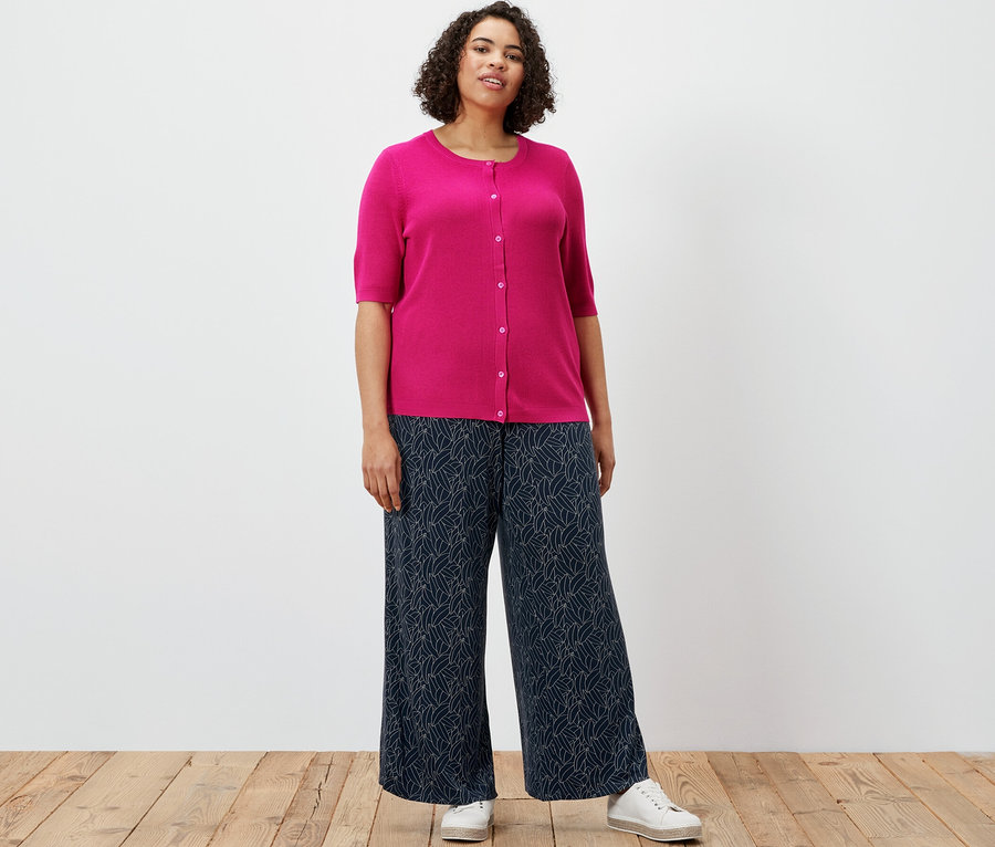 Nő visel finomkötésű kardigánt lennel és nyomott mintás palazzo nadrágot, sötétkék-krémfehér színben.