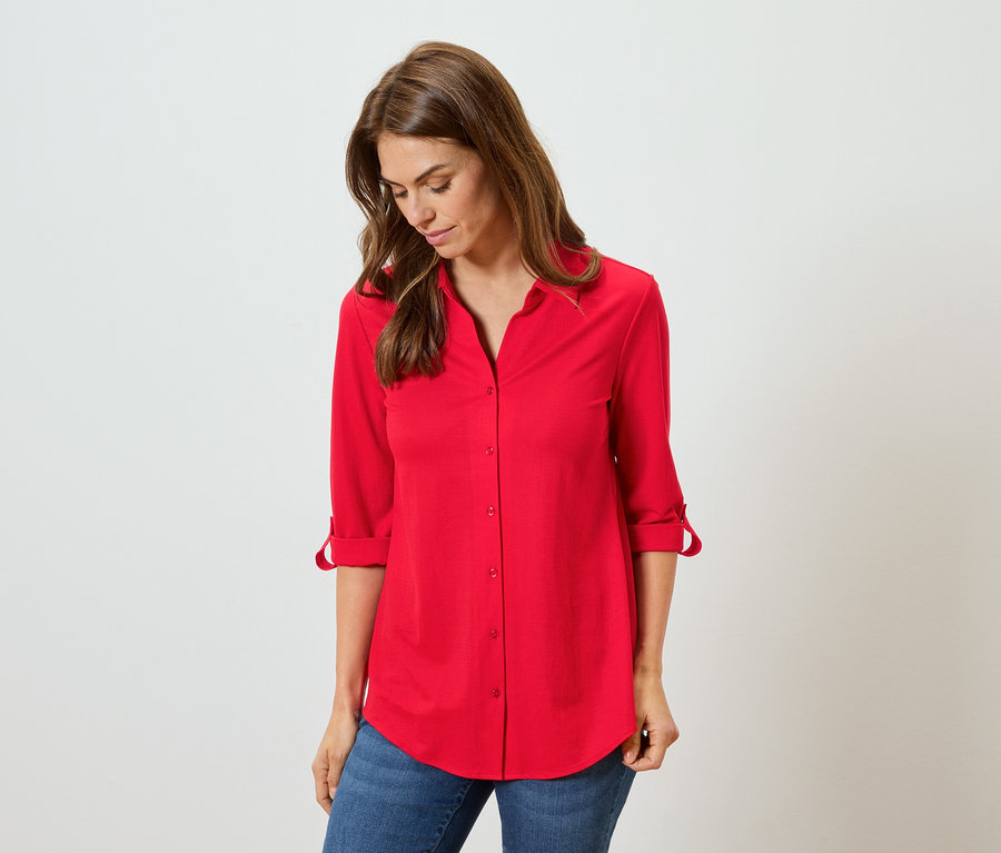 Nő visel egy piros inget és kék farmert.