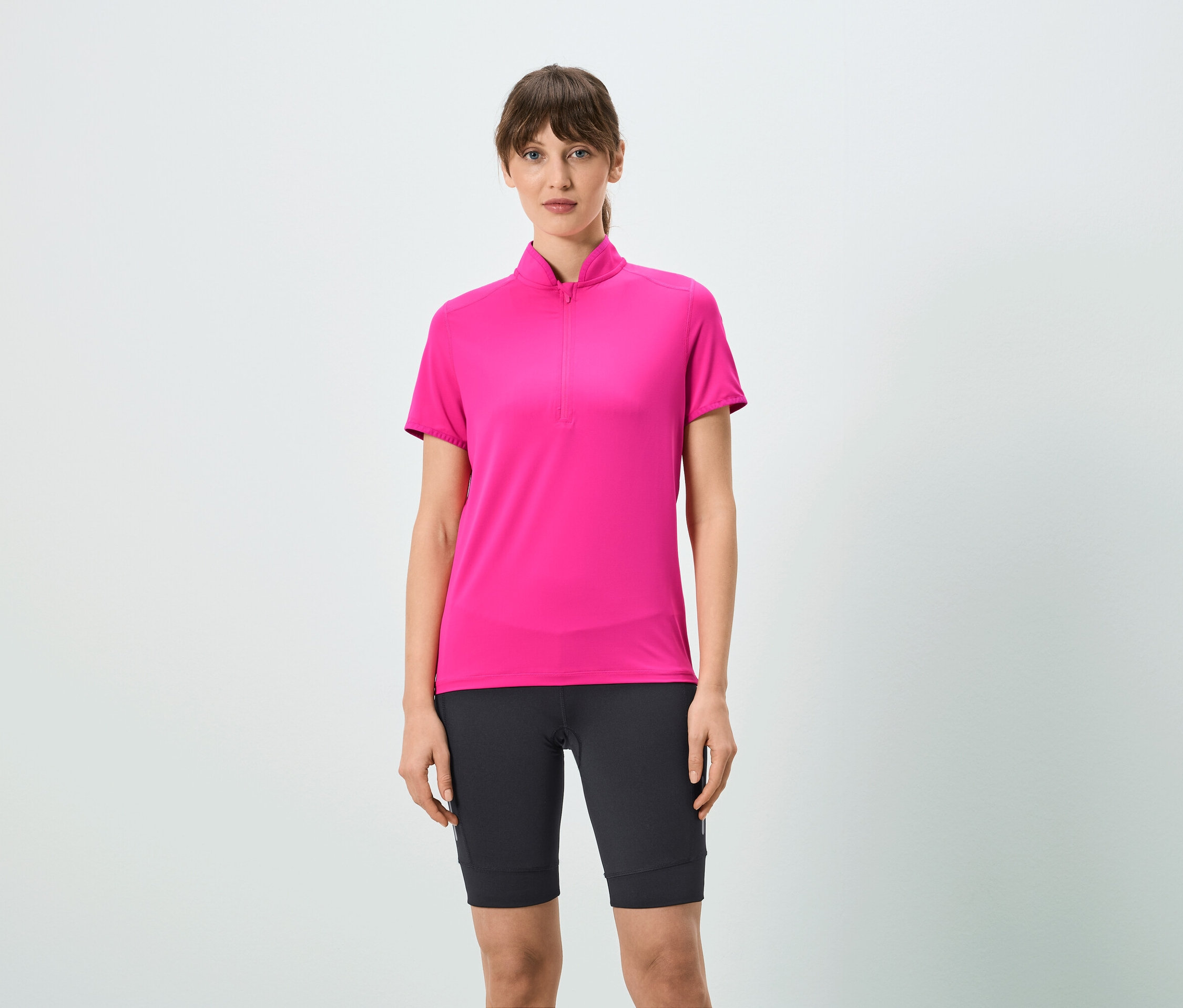 Nő visel rózsaszín, rövid cipzáras pólót és fekete rövidnadrágot.