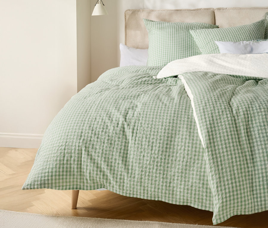 Egy ágy világoszöld-fehér kockás paplannal és hozzáillő párnákkal.