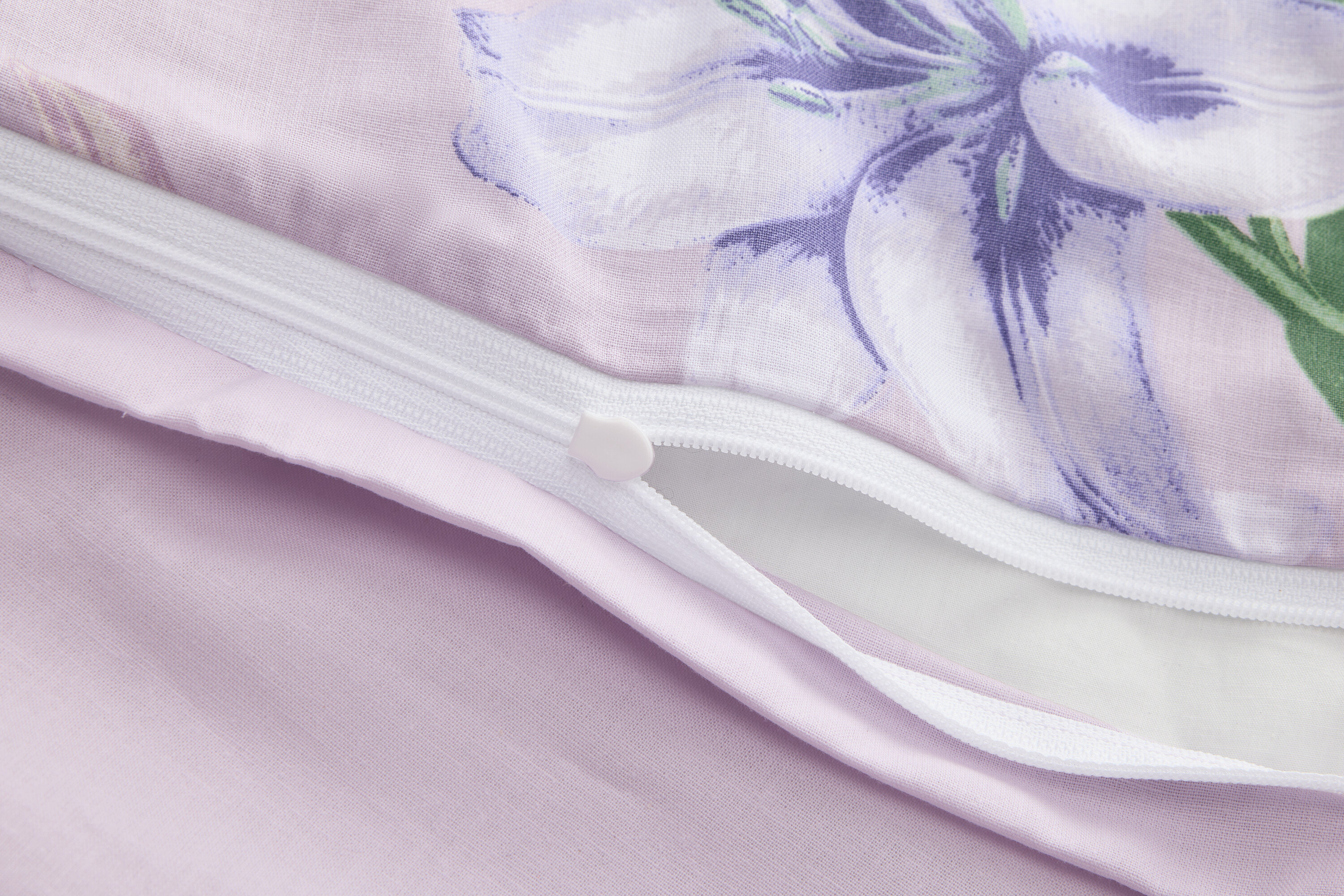 Egy részben nyitott, virágmintás, lila paplanhuzat közeli képe cipzárral.