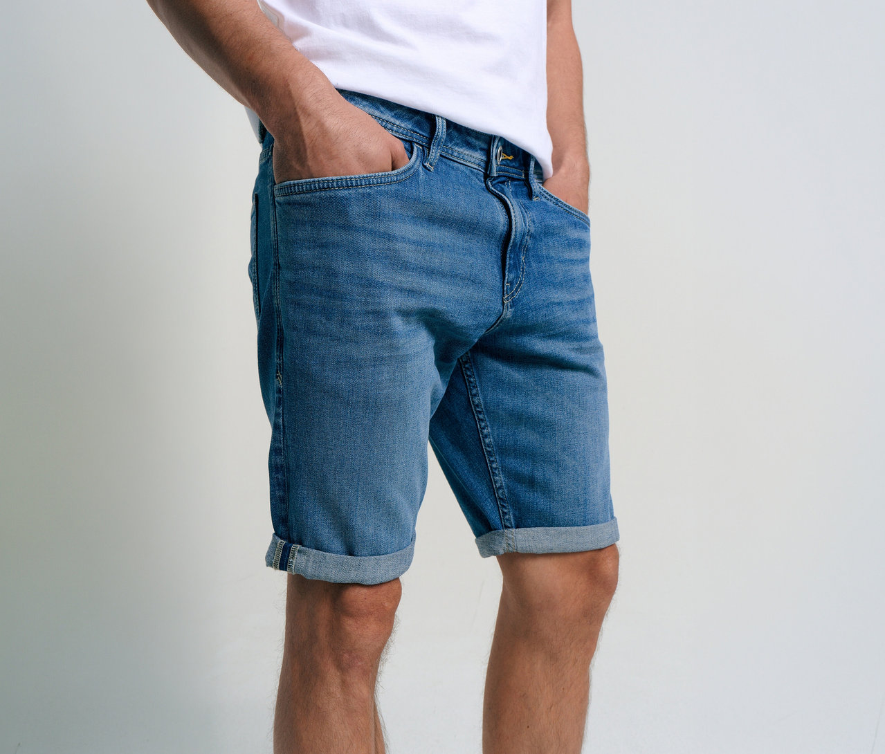 Férfi Tom Tailor TTJOSH REGULAR SLIM farmer rövidnadrágban, kőmosott középkék farmerben, kezével a zsebében.