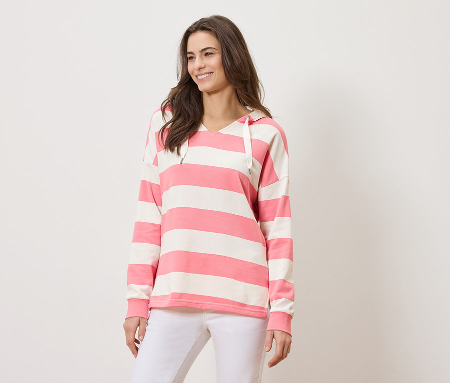 Nő rózsaszín-fehér csíkos kapucnis pulóvert és fehér nadrágot visel.