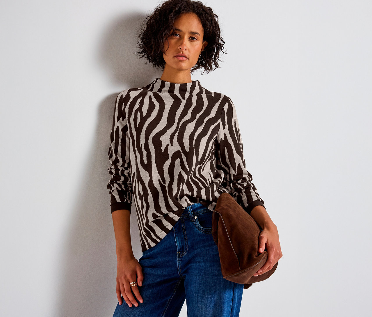 Nő visel zebra mintás Street One jacquard pólót, farmert és egy barna táskát tart.