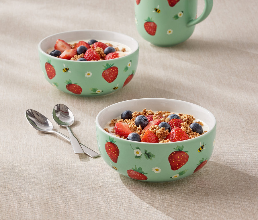 Két tál joghurttal, eperrel és áfonyával töltve, eper mintával és egy kancsó áll az asztalon.