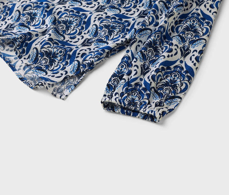 Egy fehér-kék mintás blúz ujjának közelképe.